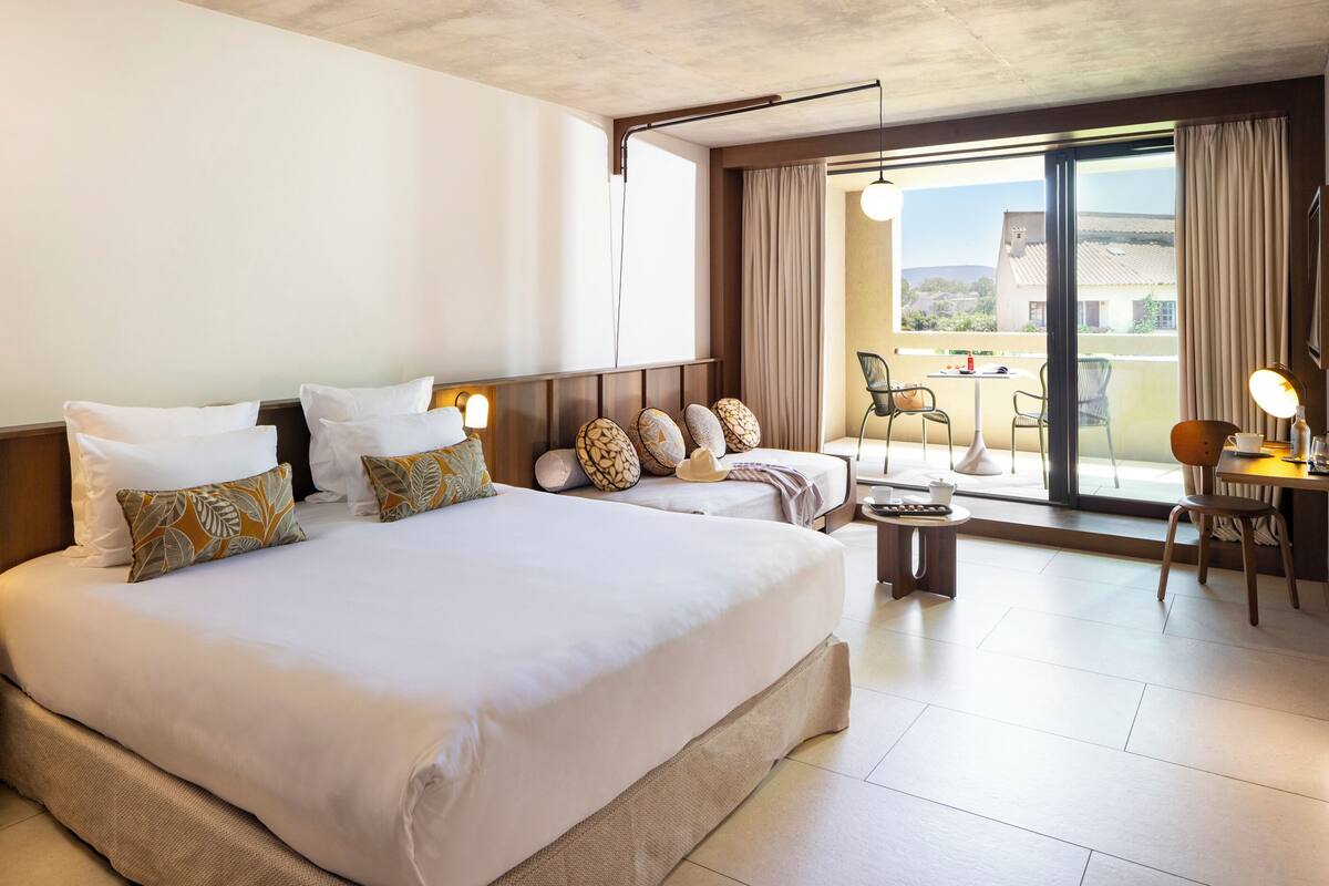 A hotel room with a large bed, a balcony with a table and chairs, and a view of the outside.