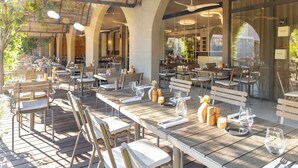 An outdoor dining area with tables and chairs, a ceiling fan, and a view of the interior through glass doors. - Son de Mar (Lecci)