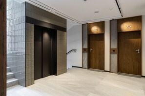 A modern elevator area with two elevators, numbered 24 and 25, and a staircase with a patterned wall. - Lion Apartments Gdansk (Gdansk)