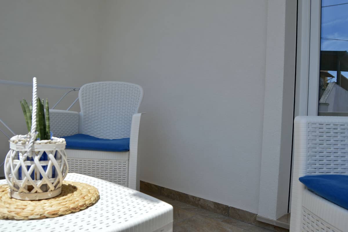 Uma cadeira de vime branca com almofada azul, um tapete de mesa tecido e um lanterna branca com corda e decoração de cactos.