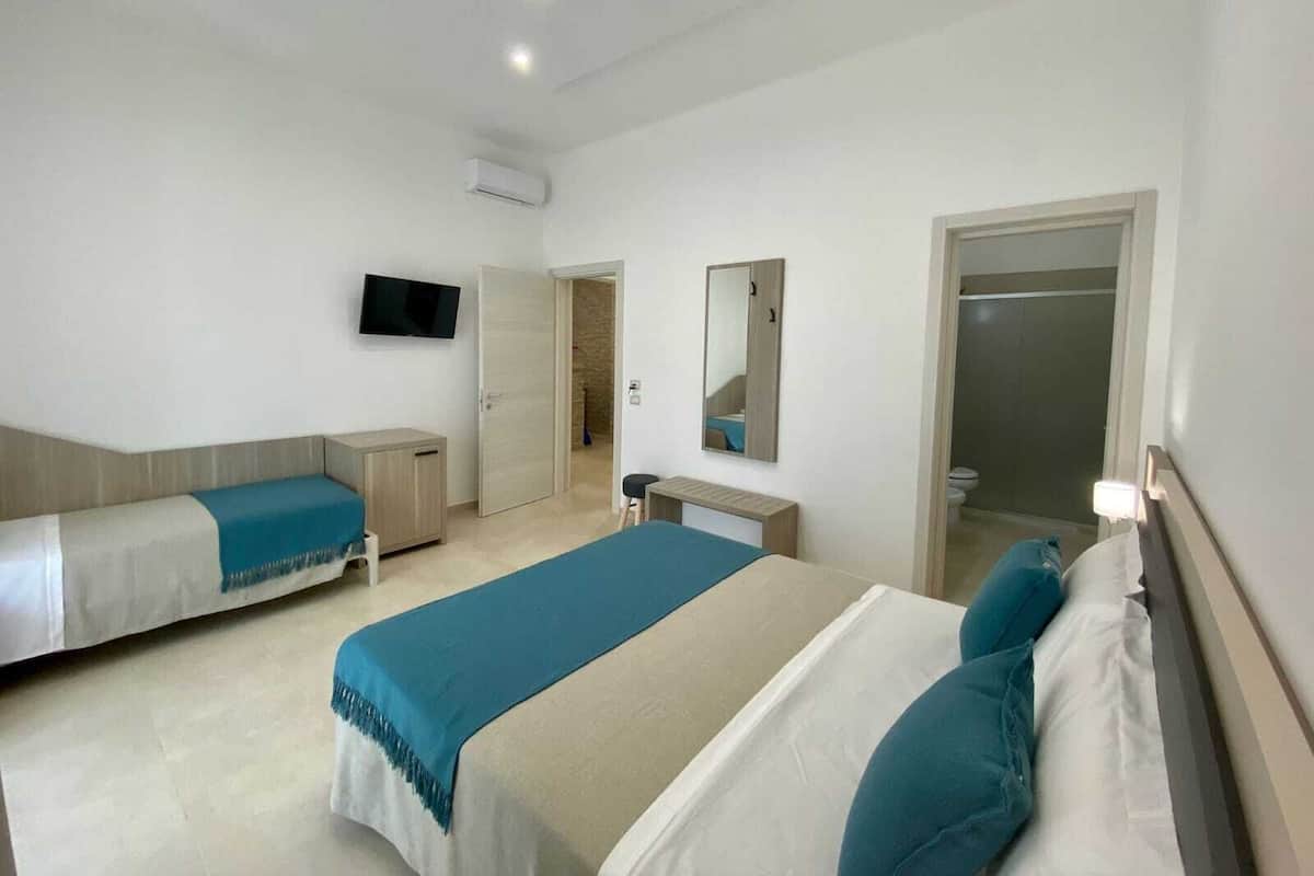 Quarto de hotel com duas camas, televisão, espelho e banheiro visível por uma porta aberta.