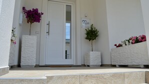 A white door with a glass panel, flanked by two white planters with flowers, and a sign above the door. - B&B MarAlè (Porto Cesareo)