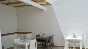 A dining area with a white table and chairs, a wooden ceiling, and a kitchen area with white cabinets and a wooden countertop. - B&B MarAlè (Porto Cesareo)