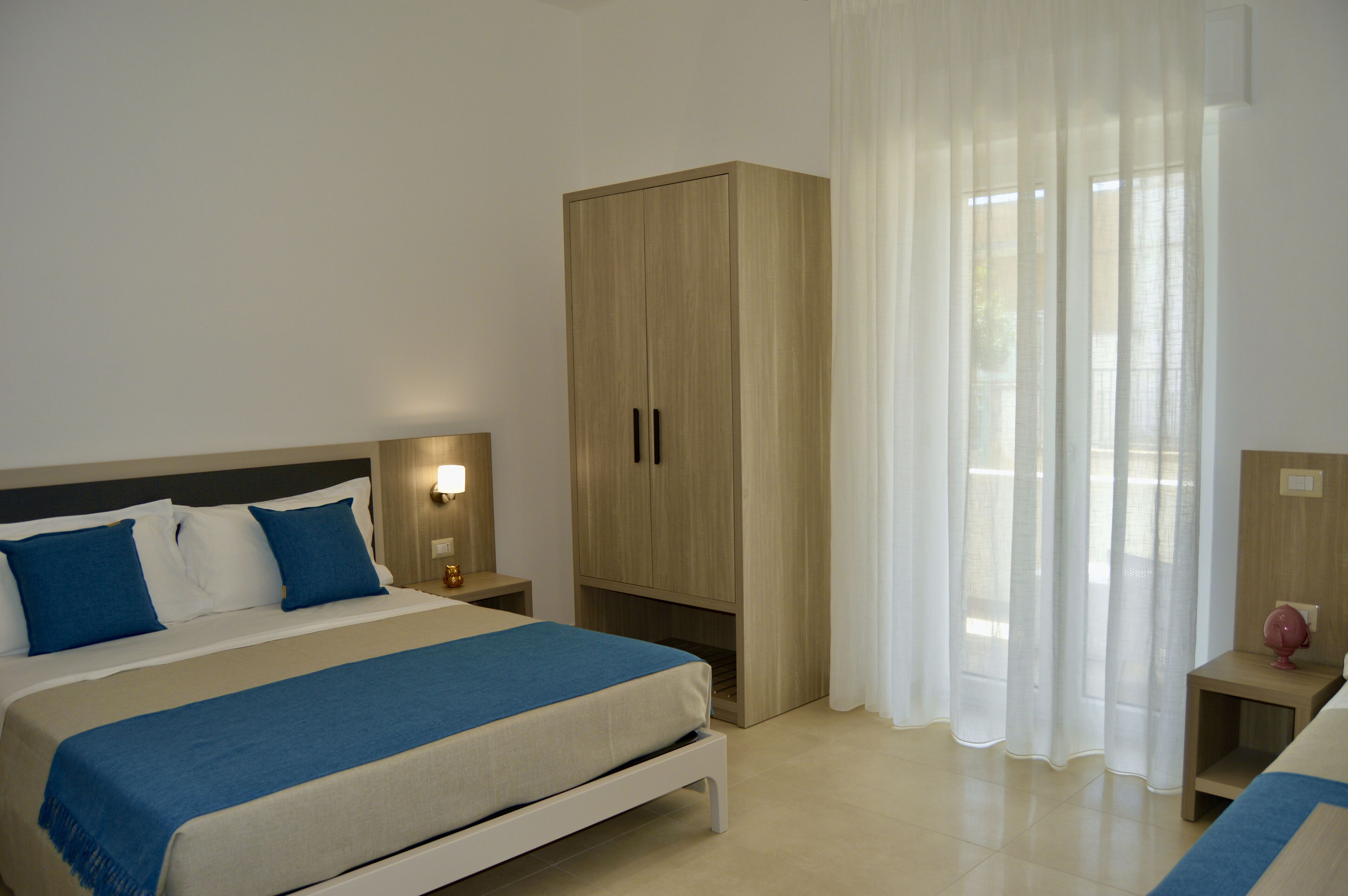 A bedroom with a bed, nightstands, a wardrobe, and sheer curtains.