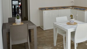 A dining area with white tables and chairs, a kitchen area with a wooden countertop, and a small potted plant on each table. - B&B MarAlè (Porto Cesareo)