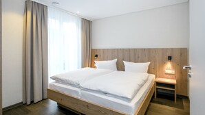 Une chambre d’hôtel moderne avec un lit en bois, deux tables de chevet et une petite table d’appoint.