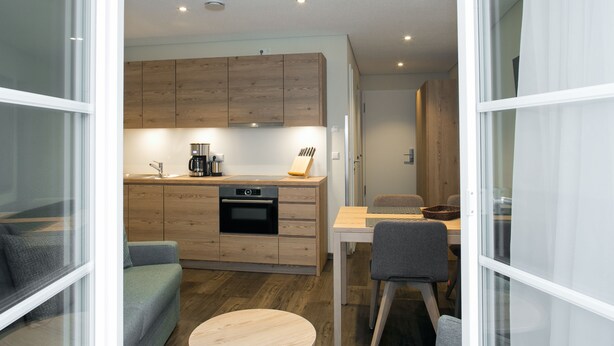 Une cuisine moderne avec des meubles en bois, un four encastré et un coin repas comprenant une table et des chaises.