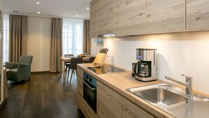 Une cuisine moderne avec des meubles en bois, un four encastré, une machine à café et un évier en acier inoxydable.