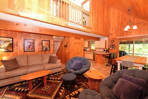 A wooden interior with a sofa, armchairs, a dining table, and a kitchen area.