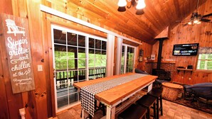 Un intérieur en bois avec une grande table, des chaises, un téléviseur et un panneau indiquant : « Sippin', grillin' and chillin' at the S. »