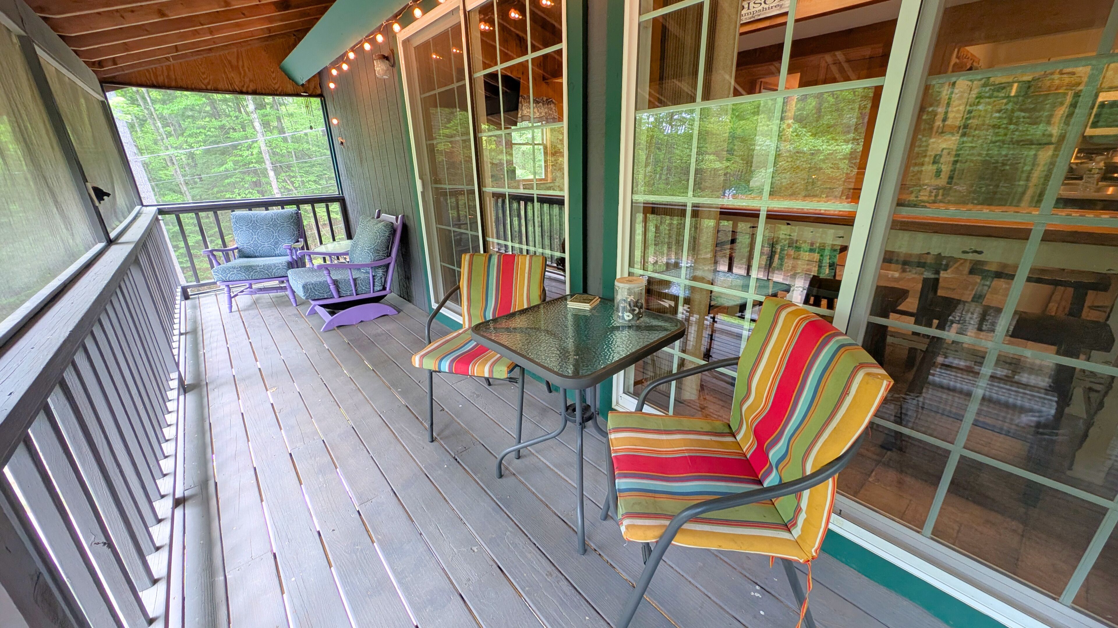 Une véranda avec une table et des chaises en verre, une terrasse en bois et une vue sur la forêt.