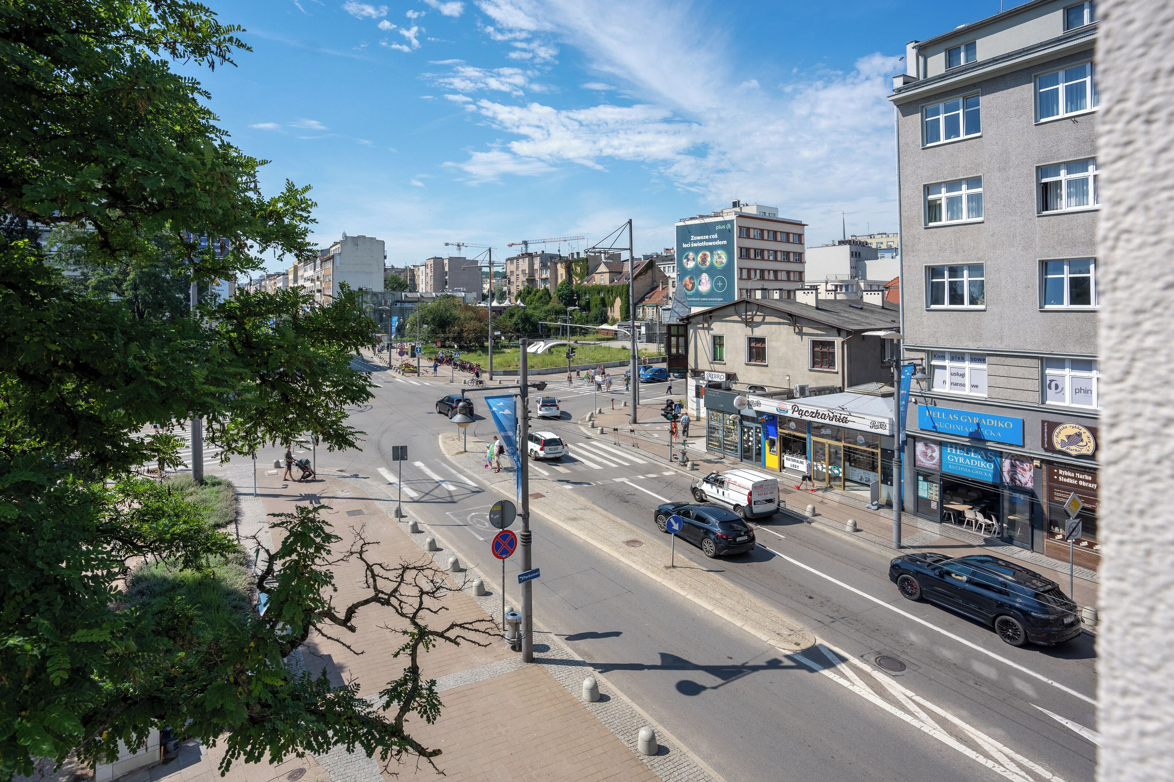 A city street with buildings, a pedestrian crossing, and a blue sign with white text.