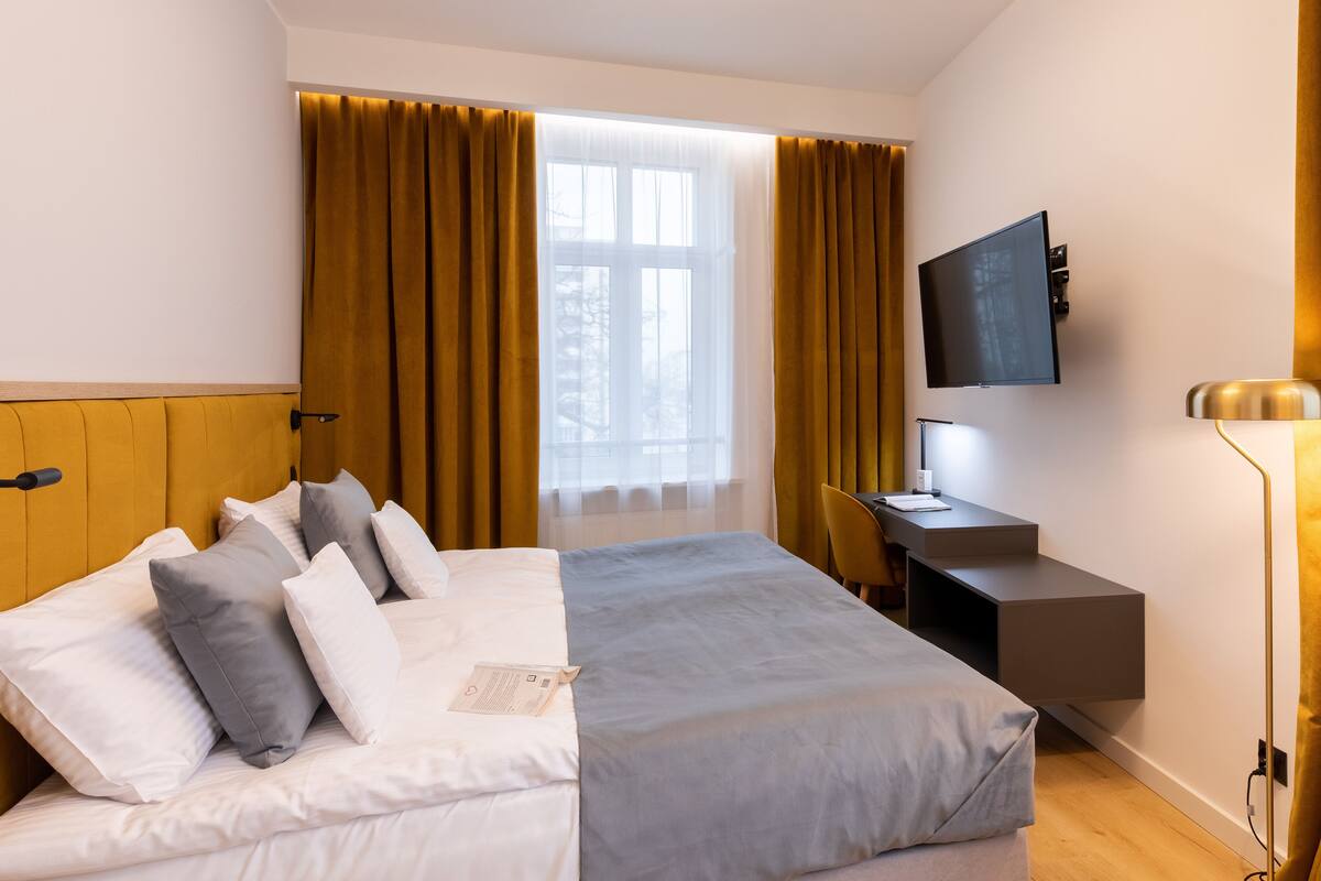 Una habitación de hotel moderna con una cama grande, un escritorio, un televisor y un ventanal con cortinas.