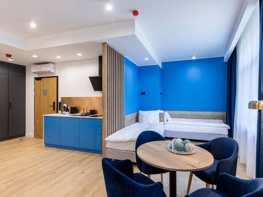 Una moderna camera d'albergo con una parete blu a contrasto, un tavolo da pranzo in legno e un'area separata con i letti.