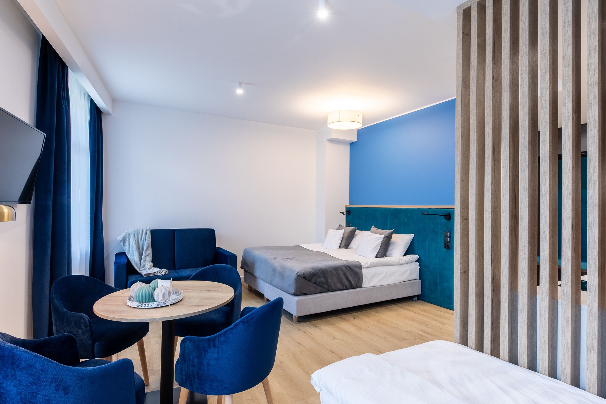 Et moderne hotelværelse med en seng, et siddeområde med stole og et bord, samt et fjernsyn monteret på væggen.