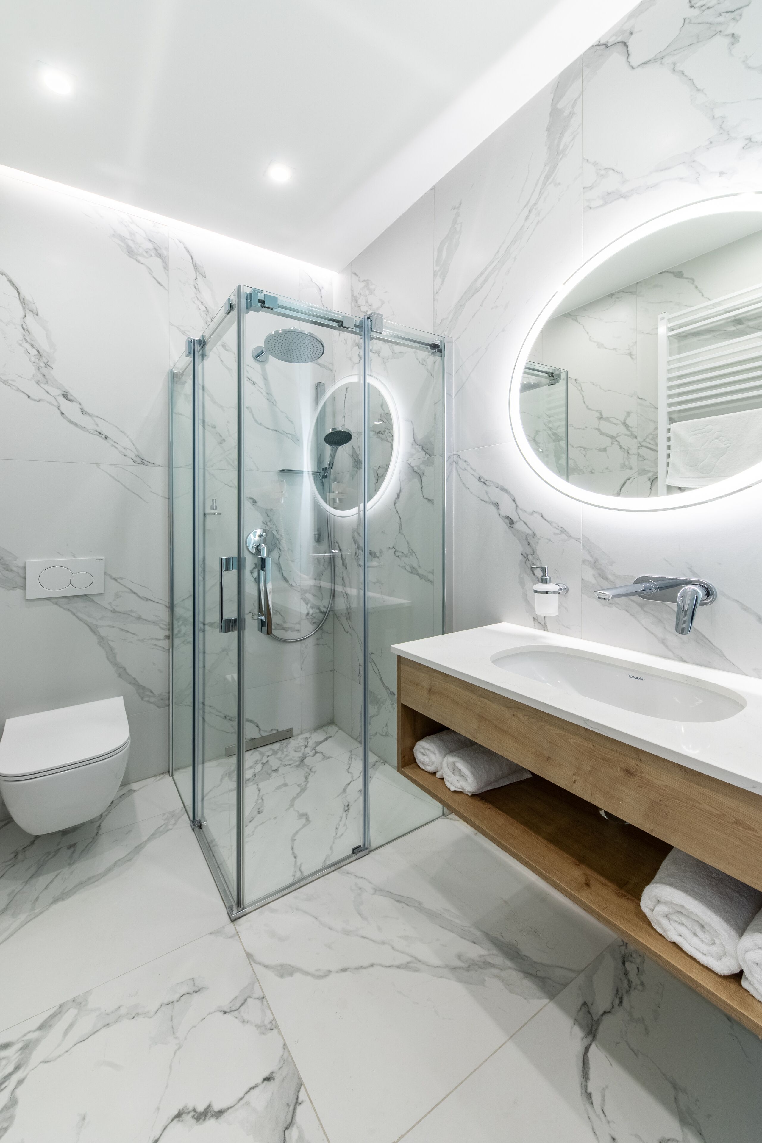 Ein modernes Badezimmer mit einer Duschkabine aus Glas, einem weißen Waschbecken und einem Boden mit Marmorfliesen.