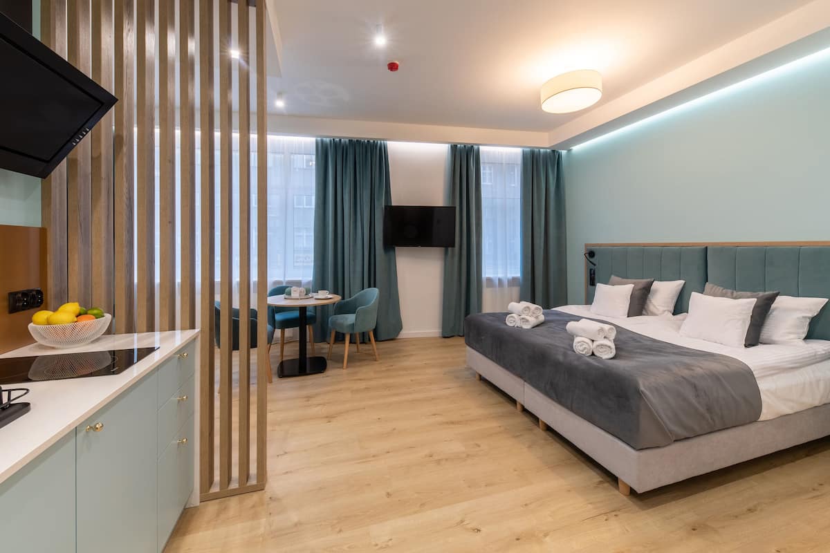 Una habitación de hotel moderna con una cama, un escritorio con un frutero, un televisor y vistas a la ciudad a través de amplios ventanales.