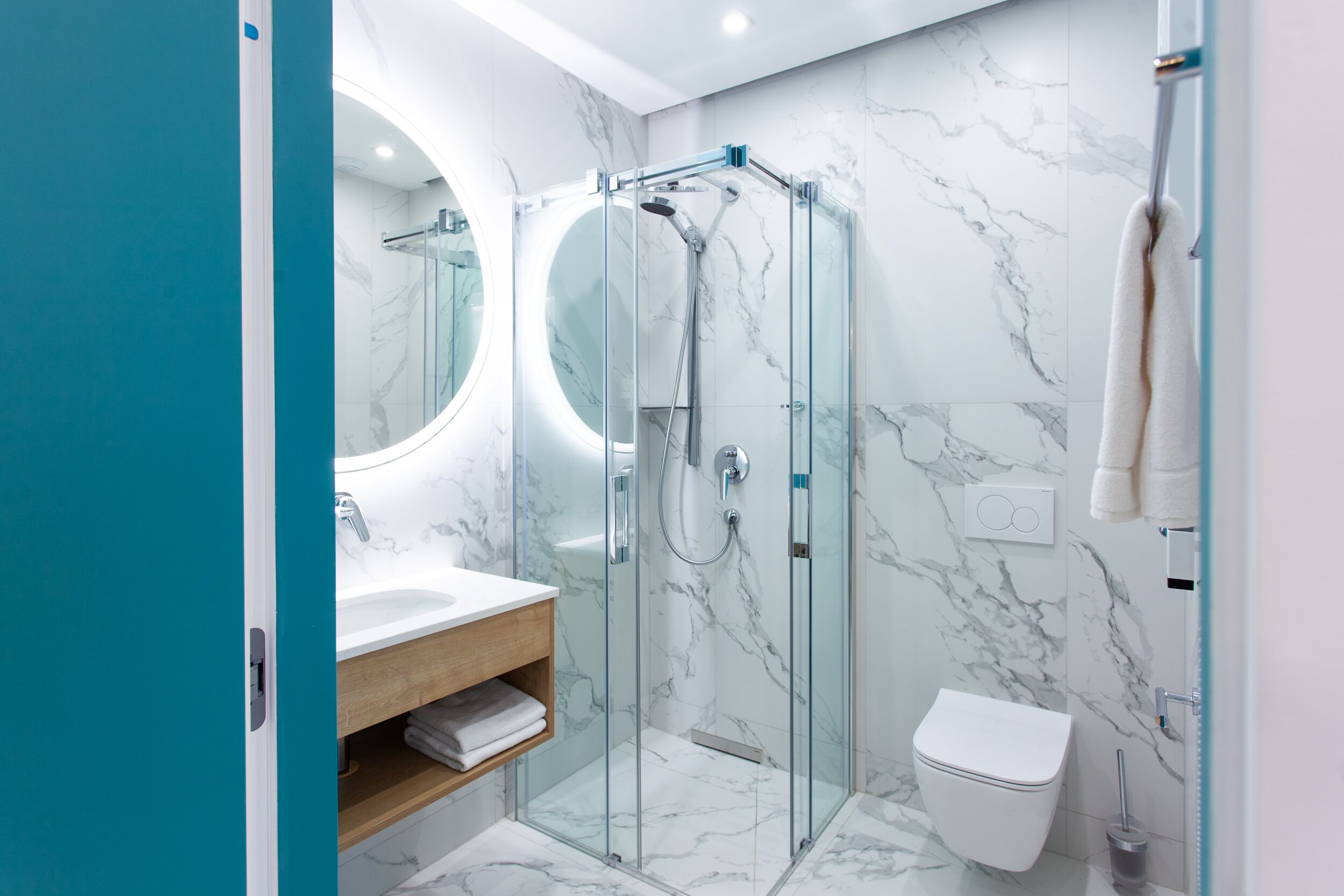 A modern bathroom with a glass-enclosed shower, a white toilet, and a marble-tiled wall.