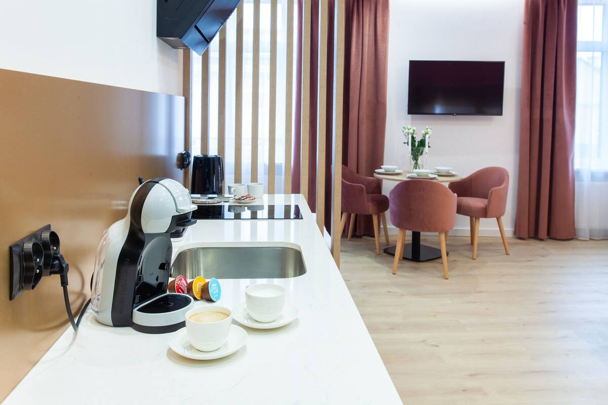 Una cocina moderna con cafetera, un comedor con mesa y sillas, y un televisor instalado en la pared.