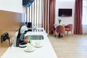 Una cocina moderna con cafetera, un comedor con mesa y sillas, y un televisor instalado en la pared.