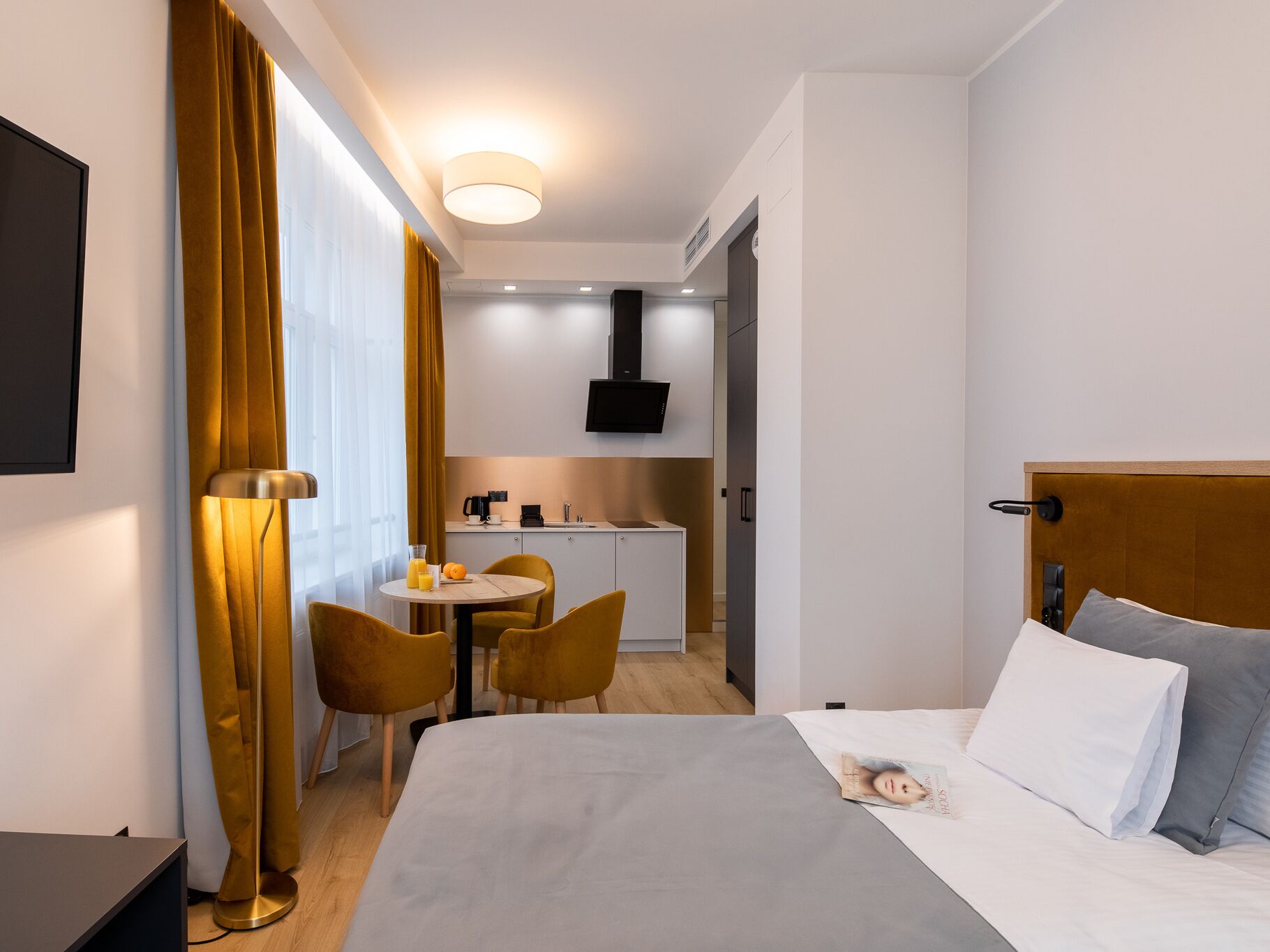 Quarto de hotel moderno com cama, escrivaninha e cozinha compacta.