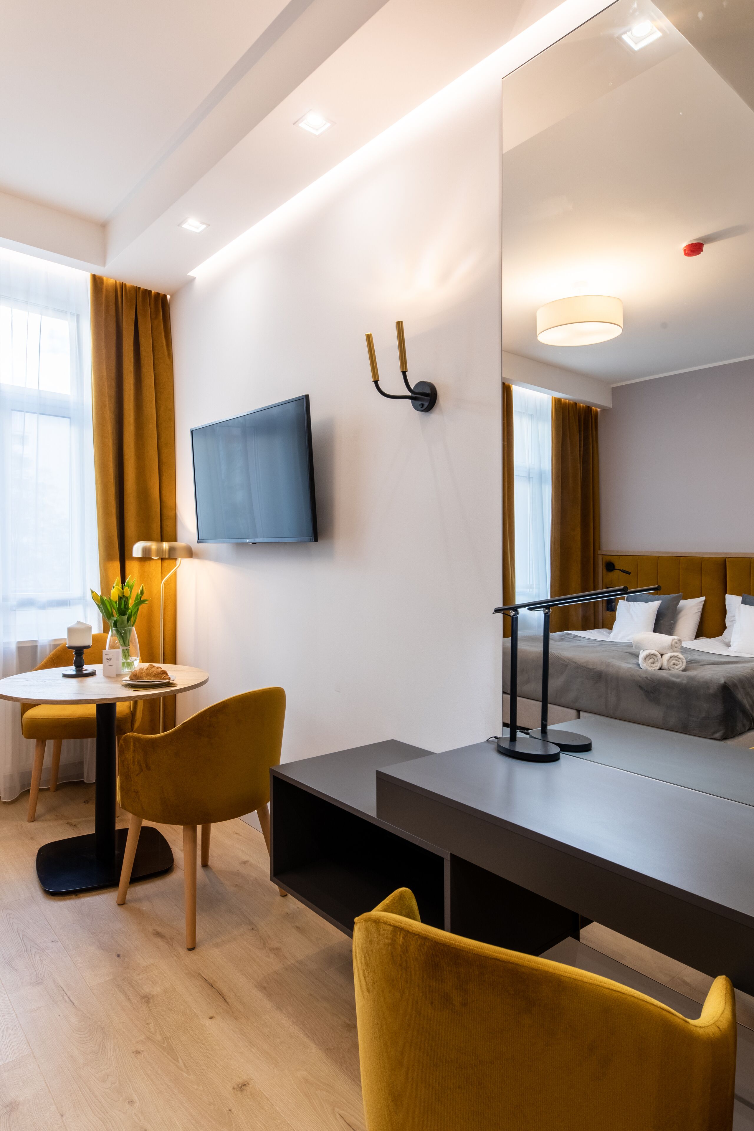 Une chambre d’hôtel moderne équipée d’un lit, d’un bureau, d’une chaise, d’une télévision et d’un grand miroir.