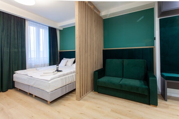 A modern hotel room with a bed, a green sofa, and a wooden partition.