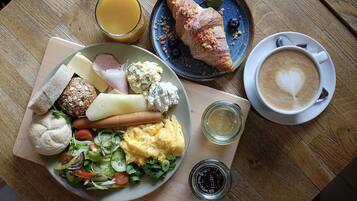 A breakfast plate with croissants, ham, cheese, and a salad, along with a cup of coffee and a glass of orange juice on a wooden table.