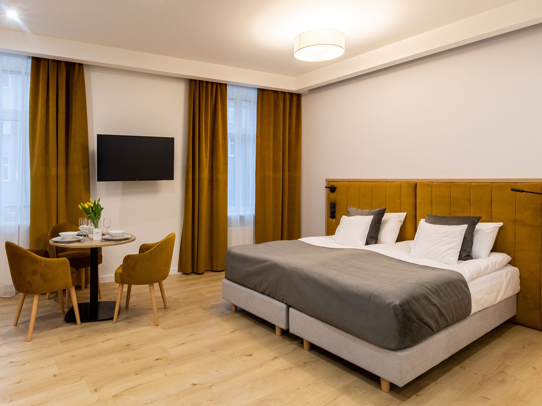 A hotel room with a bed, a desk with chairs, a TV, and a window with curtains.