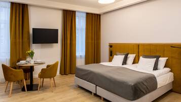 A hotel room with a bed, a desk with chairs, a TV, and a window with curtains.