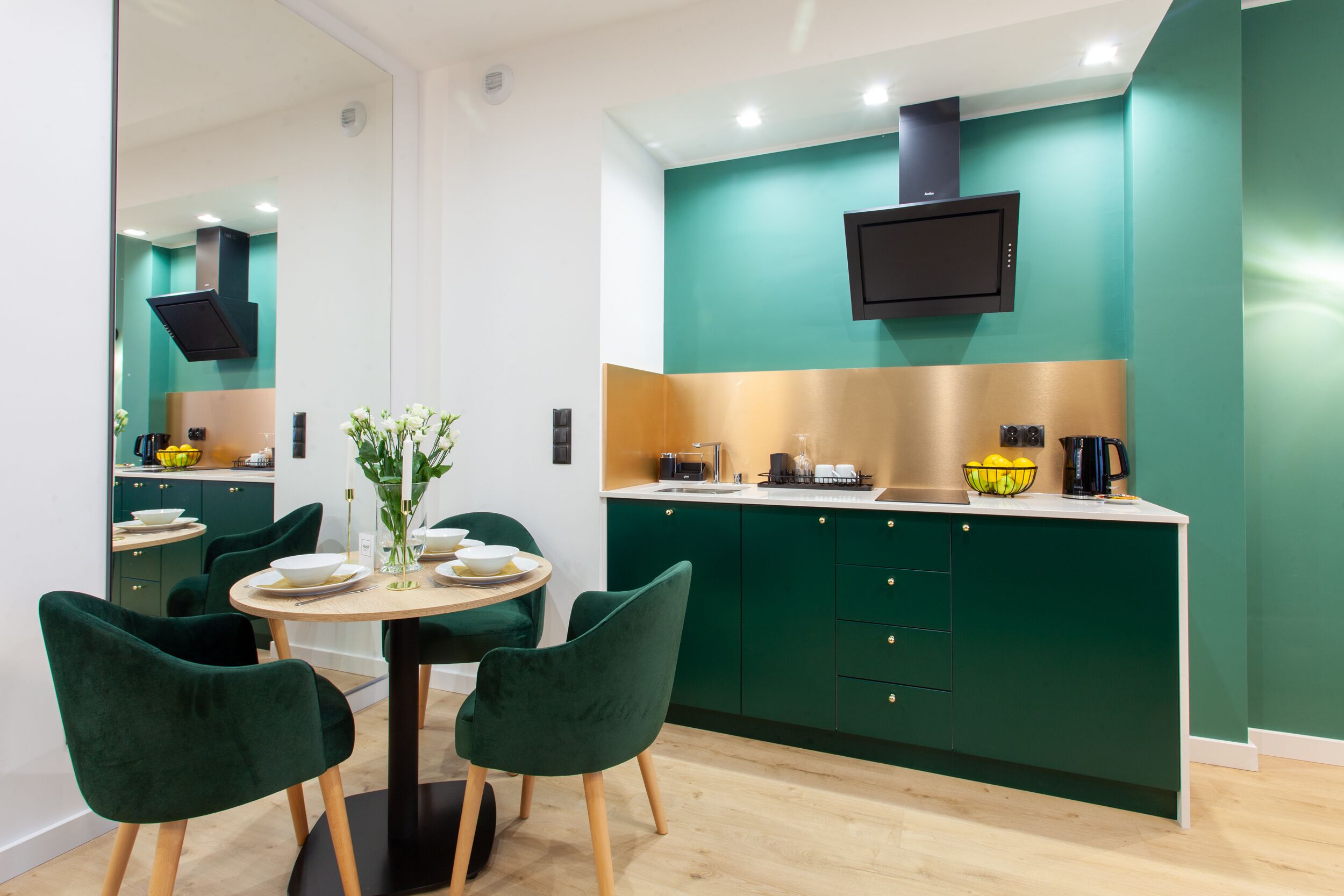 Una cocina moderna con armarios color turquesa, una mesa redonda con sillas y un televisor empotrado sobre la encimera.