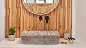 A bathroom with a wooden wall, a round mirror, a stone sink, and a small potted plant.