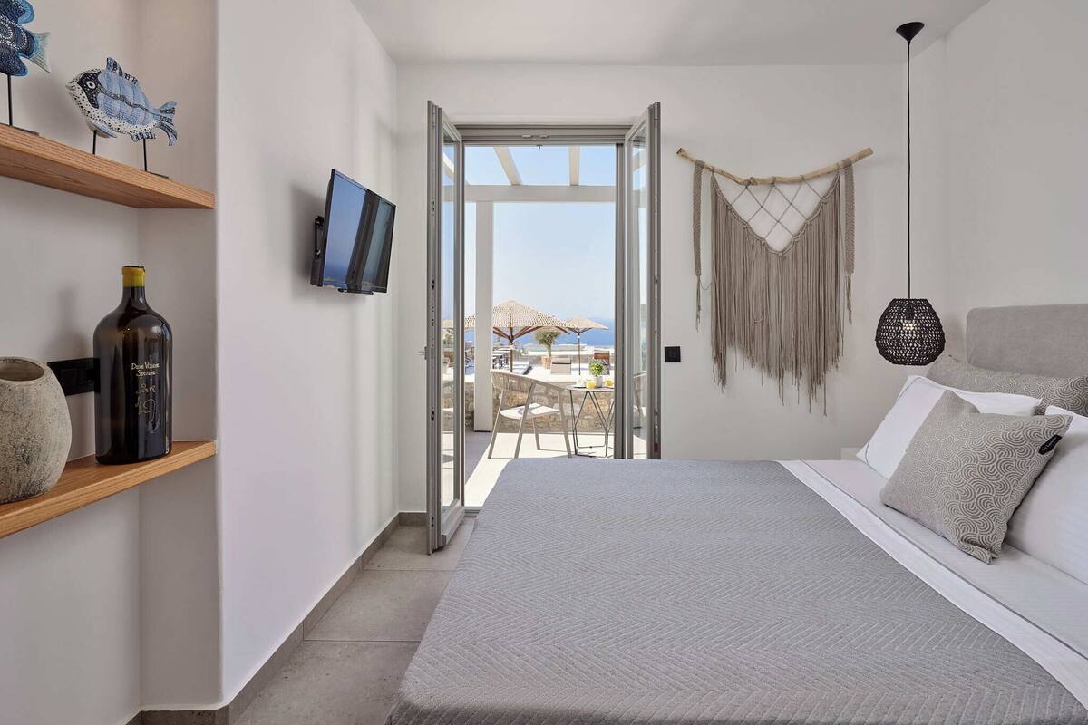 Un dormitorio con una cama, televisor, botella, estante y vista al exterior.