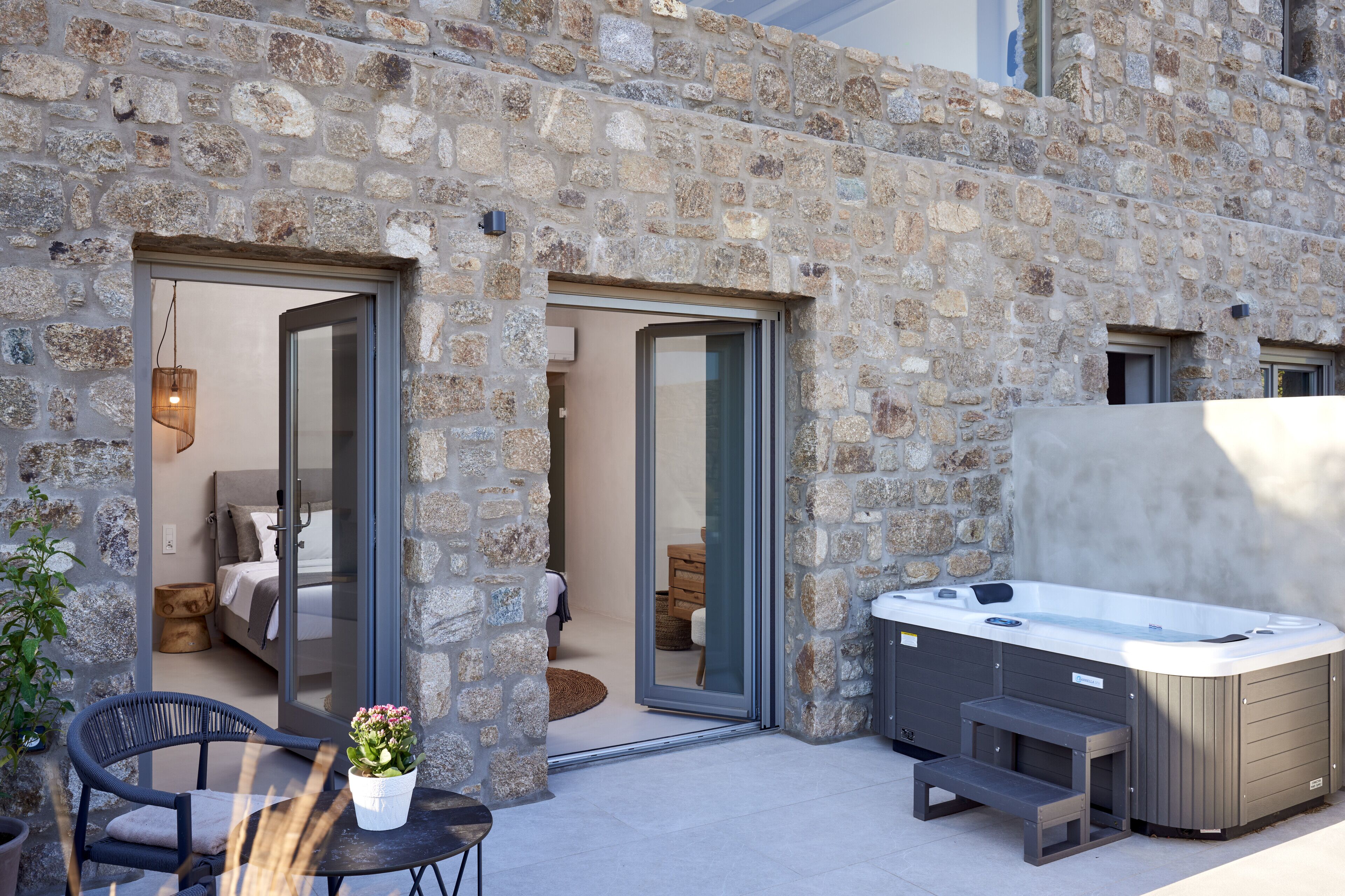 A stone building with a hot tub, a dining area, and a bedroom visible through the doors.
