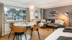 Una sala de estar moderna con un sofá, una mesa de comedor con sillas y vistas a la calle.