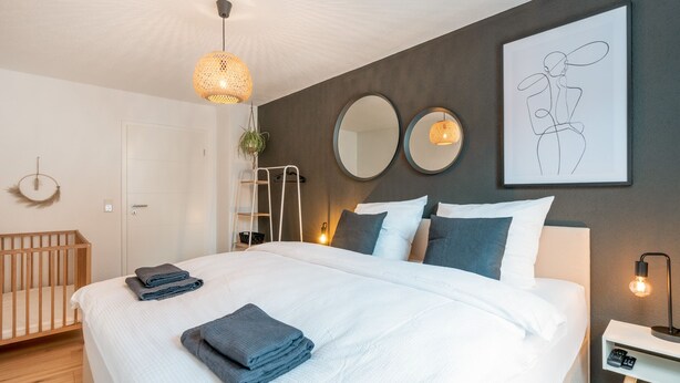 Un dormitorio moderno con una cama, mesitas de noche, una planta colgante y cuadros en la pared.