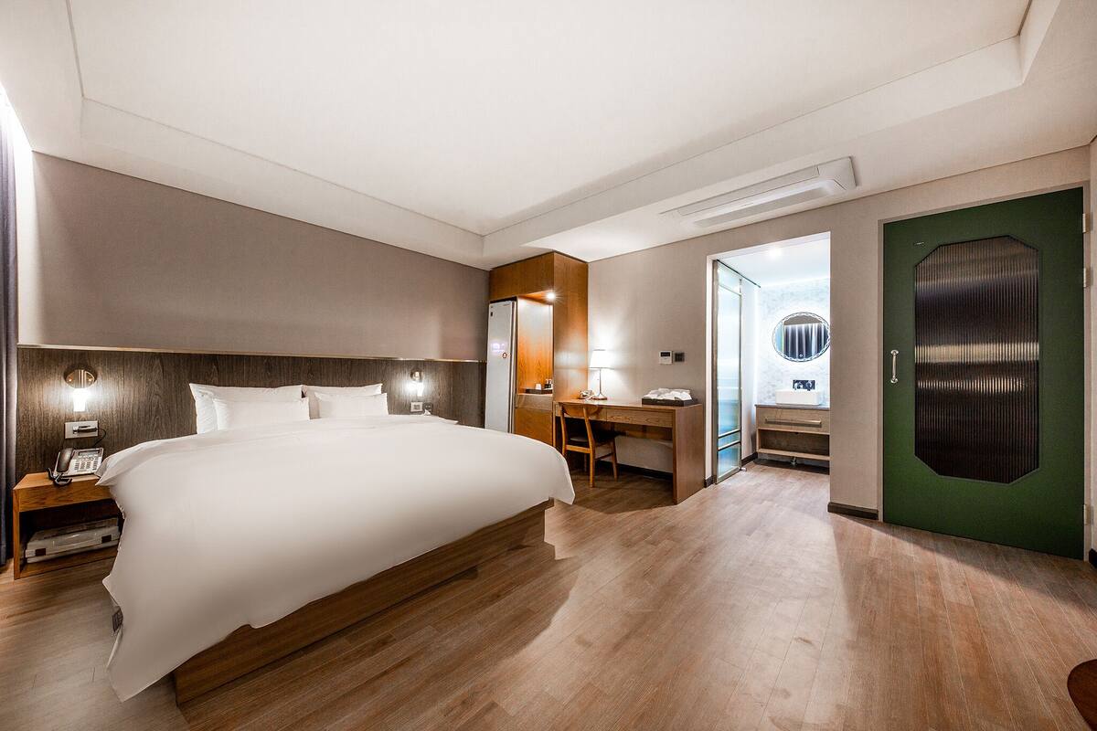Une chambre d’hôtel avec un grand lit, un bureau, une chaise, un téléphone et une porte verte.