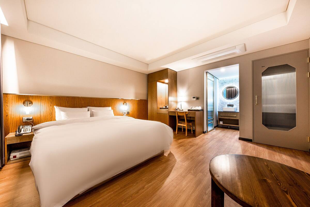 Une chambre d’hôtel avec un grand lit, un bureau avec une chaise, un téléphone et une armoire avec un miroir.