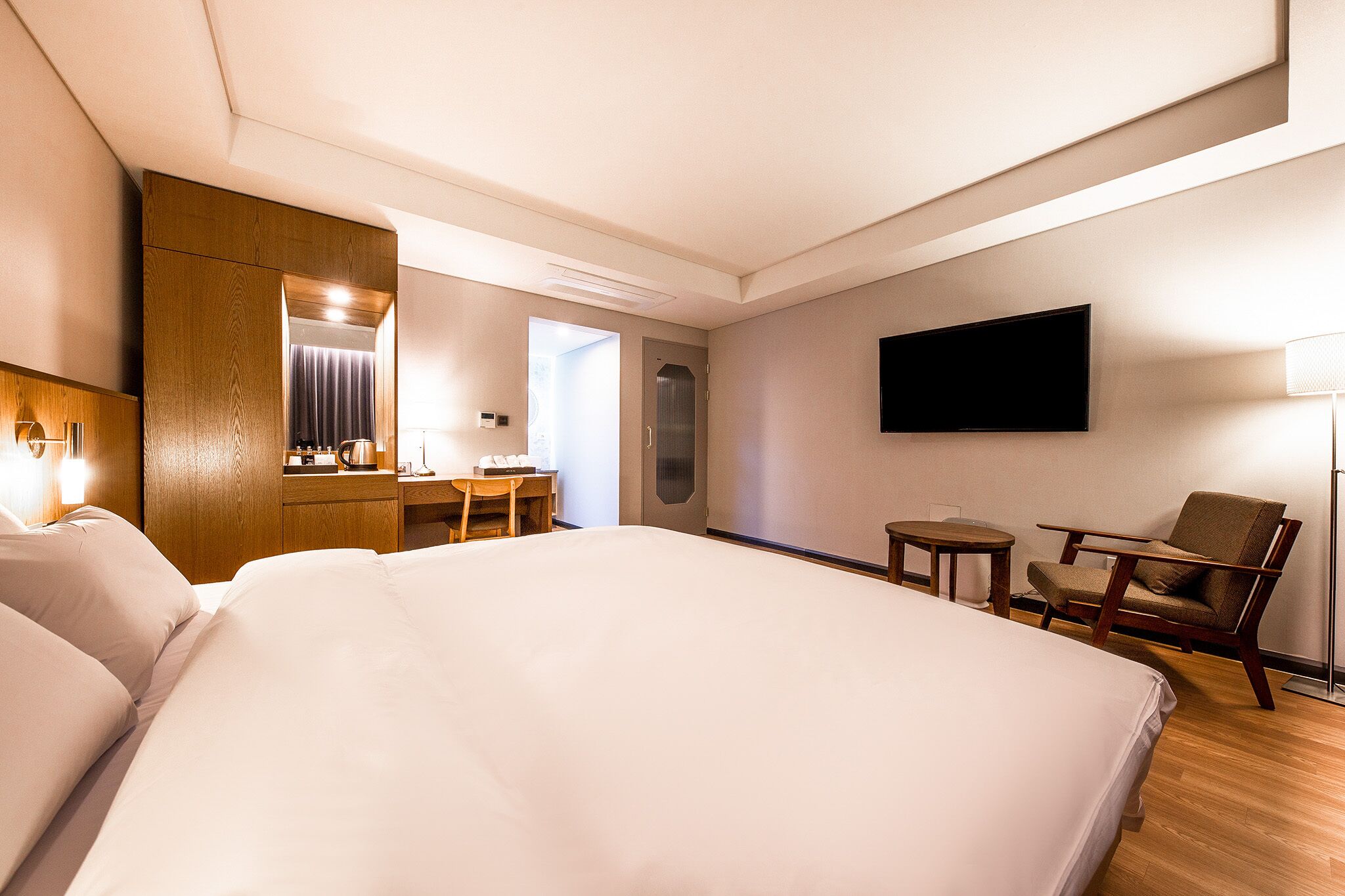 A hotel room with a large bed, a desk with a chair, a television mounted on the wall, and a lamp.