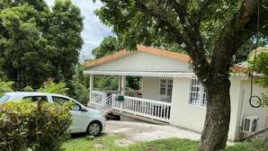 Ein Haus mit einer Veranda, ein Auto vor der Tür und ein Baum im Vordergrund.
