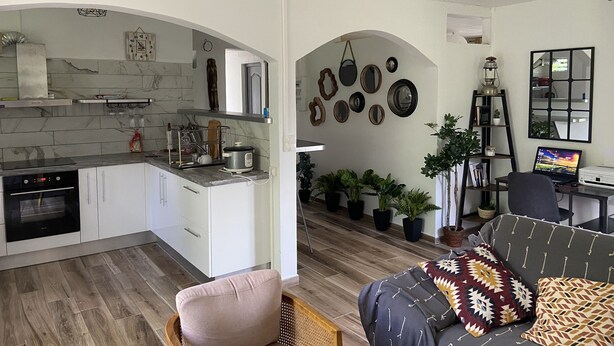 Eine moderne Küche mit weißen Schränken, einem Backofen und einem Kochfeld. Es gibt einen Essbereich mit einer Couch und einem Laptop auf einem Schreibtisch.