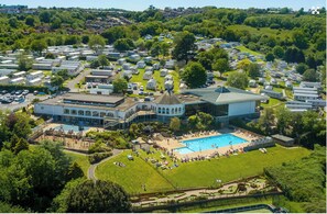 Un camping grande con varias caravanas y remolques, piscina y un edificio central con techo abovedado.