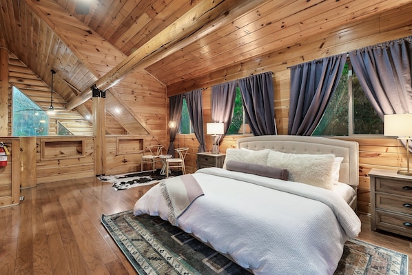 Un dormitorio de cabaña de madera acogedor, con una cama grande, una mesita de noche y un ventanal con cortinas.