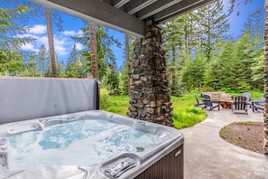 Relax in the hot tub surrounded by a serene landscape and a seating area with a table and chairs.