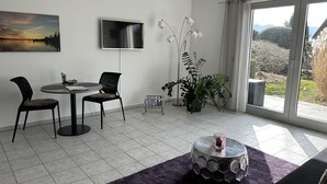 Una sala de estar moderna con comedor, un ventanal con vistas al exterior y un televisor de pantalla plana montado en la pared.