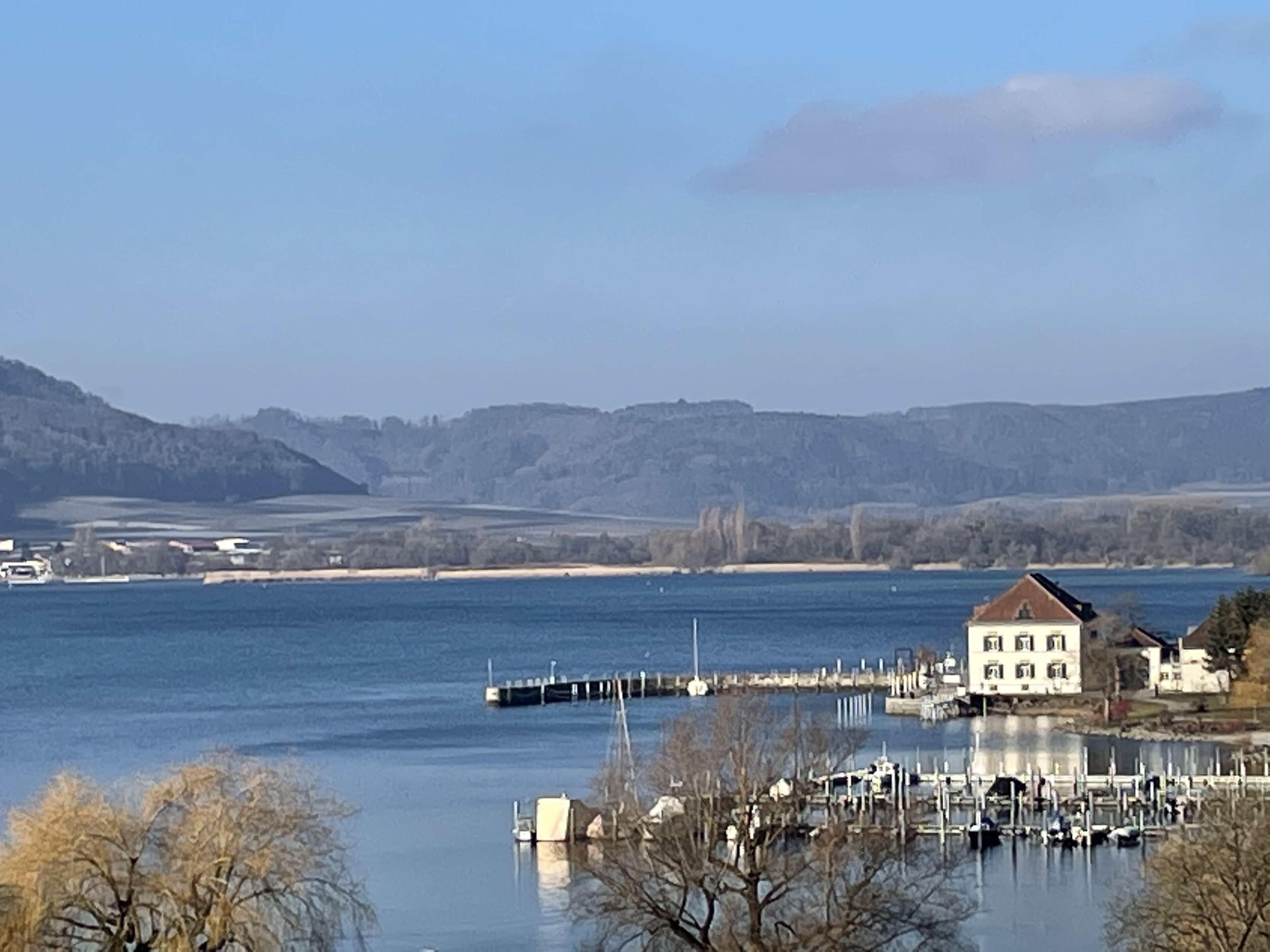 A lakeside view with a dock, a building, and distant hills.