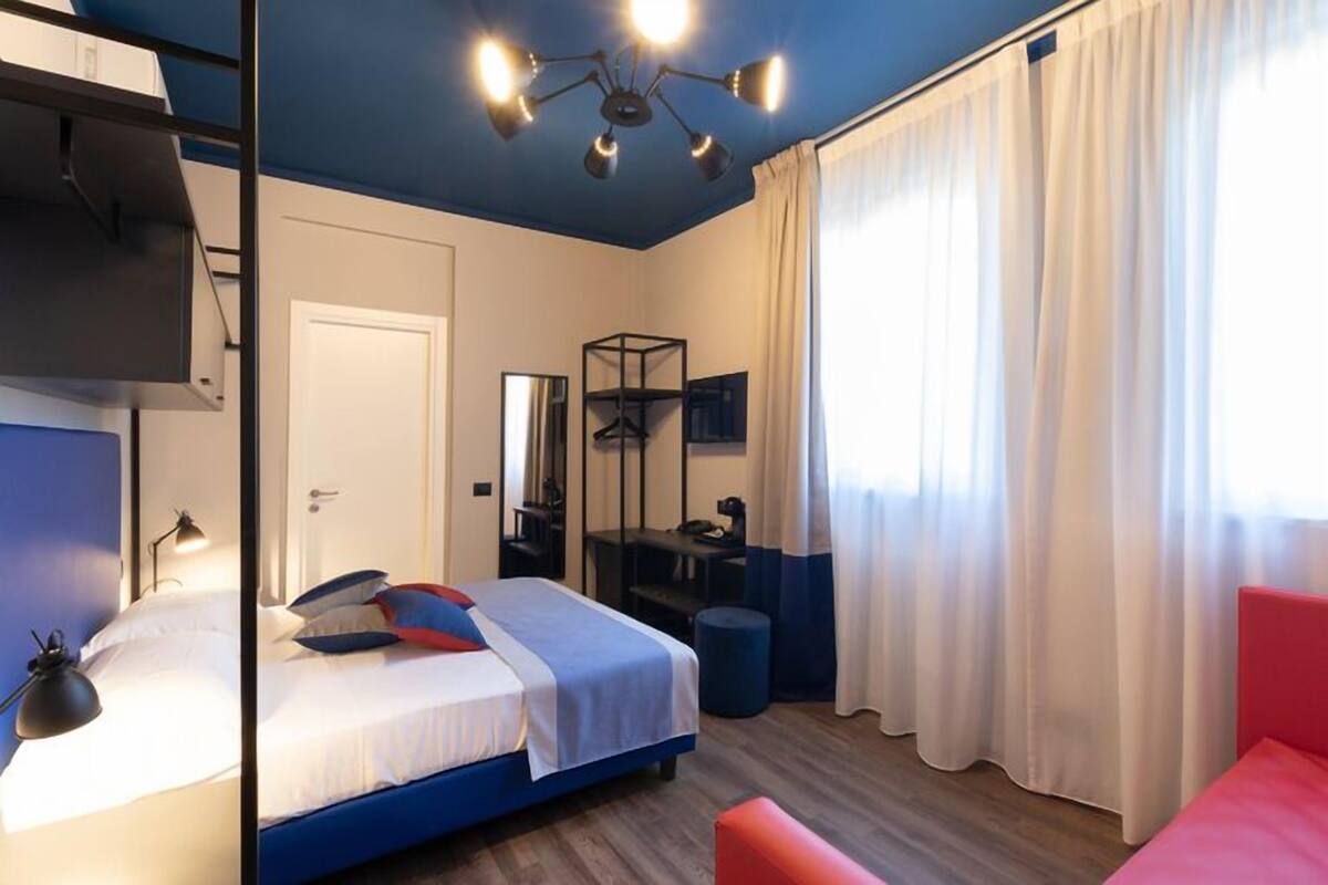 A bedroom with a bed, bedside table, lamp, and a desk with a chair.