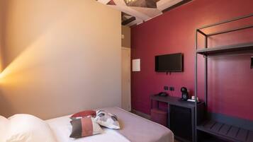Une chambre d’hôtel comprenant un lit, un bureau avec une chaise, un téléviseur fixé au mur et un mur d’accent de couleur rouge.