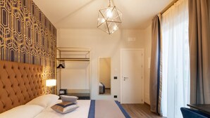 A hotel room with a tufted headboard, a large bed, a geometric-patterned wall, a hanging light fixture, and a view of a door and window with curtains. - The Time Home&Hotel (Santa Margherita Ligure)