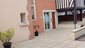 Une cour avec un sol carrelé, un bâtiment dont la structure combine des éléments en brique et en bois, et des plantes en pot.